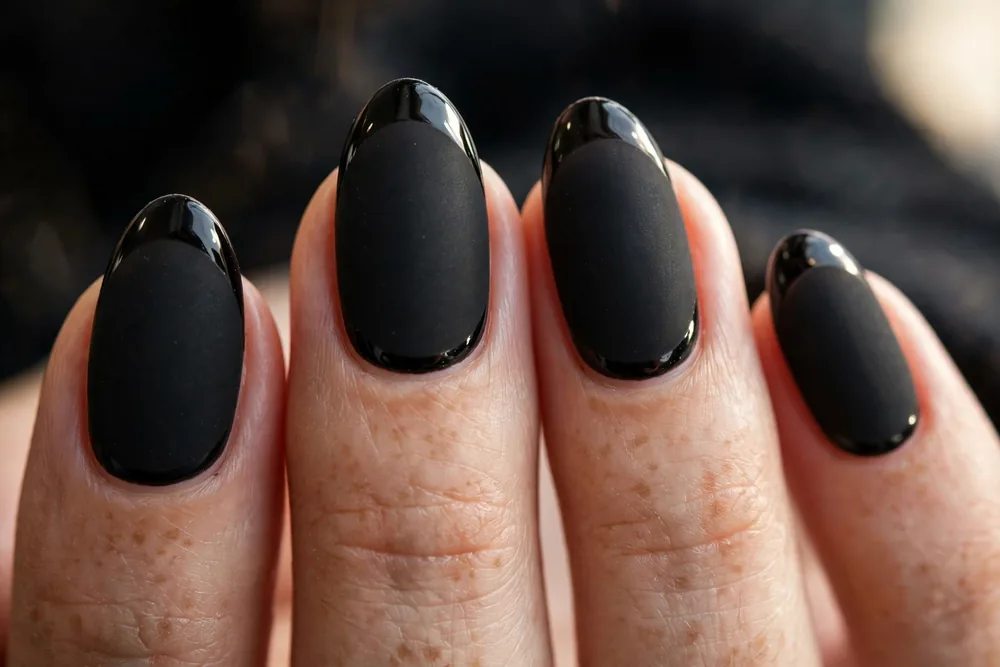 Matte black nails with glossy black French tips catching the light